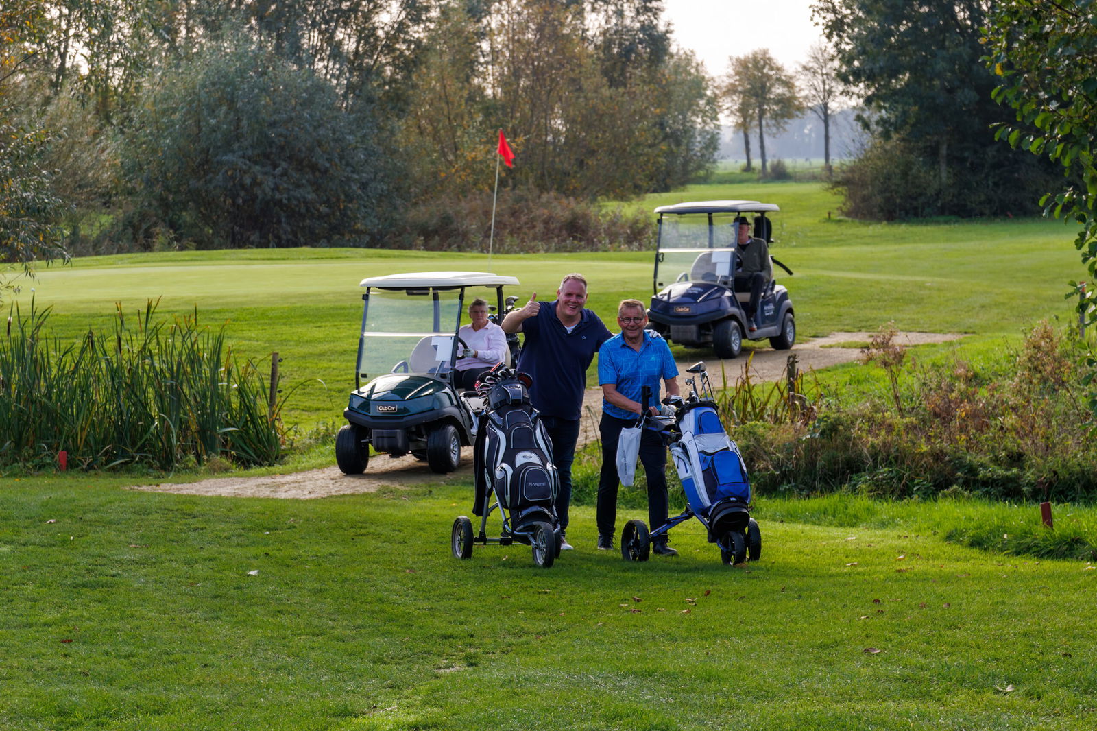 Golfers lopen met trolleys en golfkarren over de golfbaan van Golfpark Almkreek
